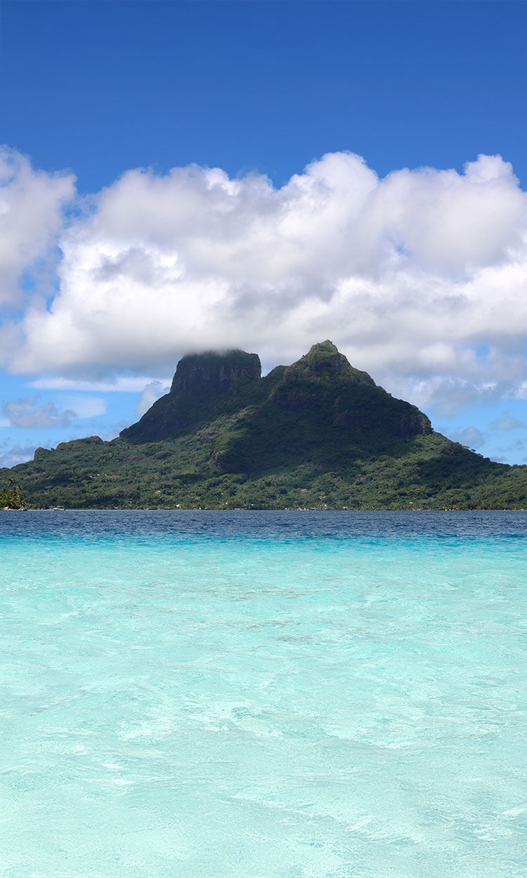 Tropical island with lush green mountains by a crystal-clear turquoise lagoon.
